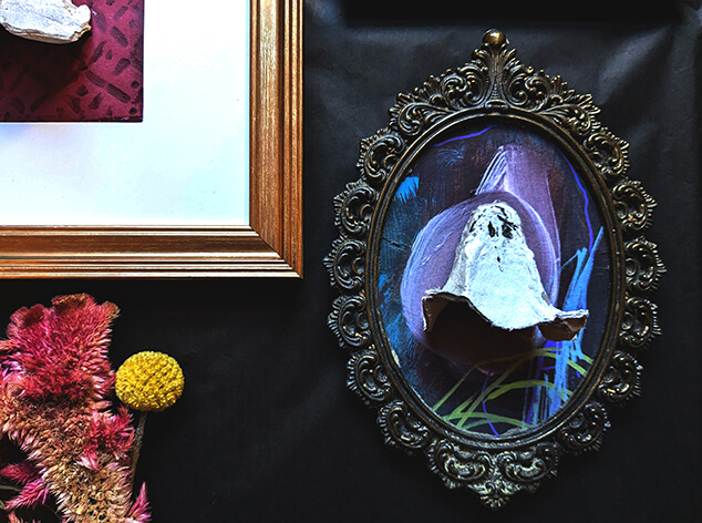 a egg carton ghost is glued to a colorful background and placed in an ornate frame